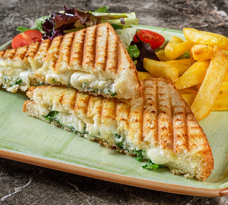 Auf einem eckigen Teller liegen zwei Panini mit Brokkoli und Käse gefüllt, außerdem Salat und Fritten. | © Getty Images/ BURCU ATALAY TANKUT