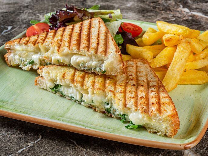 Auf einem eckigen Teller liegen zwei Panini mit Brokkoli und Käse gefüllt, außerdem Salat und Fritten. | © Getty Images/ BURCU ATALAY TANKUT