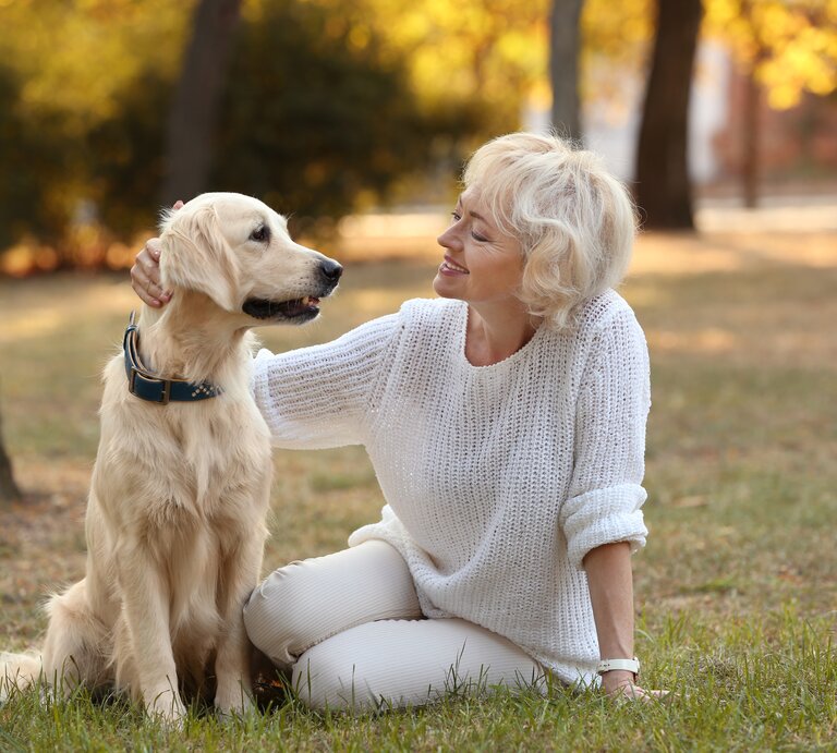 Reife Frau sitzt neben ihrem Hund und streichelt seinen Kopf. | © Shutterstock/Africa Studio