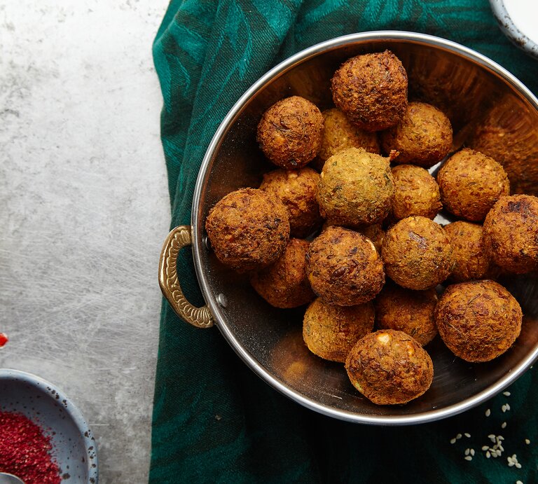 Eine silberne Schale gefüllt mit Maronen-Falafel mit Cranberrys neben einer Schüssel mit roten Gewürz, einer ausgepressten Zitronenhälfte und einer Schüssel mit einem Joghurt-Dip, vor einem dunkel grün und grauen Hintergrund, von oben.  | © Getty Images/ AnastasiaNurullina