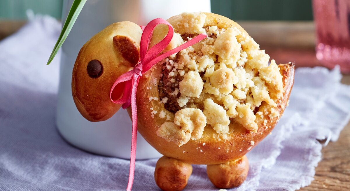 Eins der Streusel-Lämmer aufrecht und mit Schleife vor einer Blumenvase.
