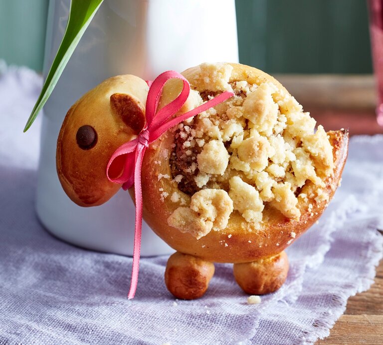 Eins der Streusel-Lämmer aufrecht und mit Schleife vor einer Blumenvase. | © EAT CLUB / Isabell Triemer
