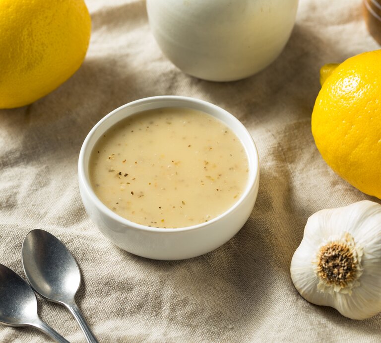 Eine Schale Zitronen-Knoblauch-Vinaigrette, zwei Zitronen, ein Knoblauch und zwei Löffeln liegen auf einem großen Leinentuch. | © Getty Images / hofack2