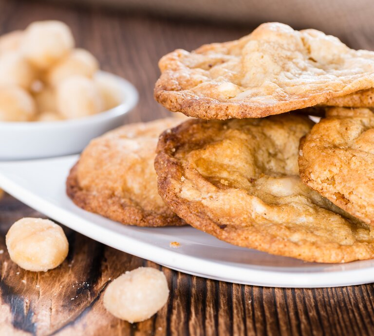 Mehrere Cookies auf einem weißen Teller und Holztisch aus seitlicher Perspektive fotografiert. | © Shutterstock/ HandmadePictures 