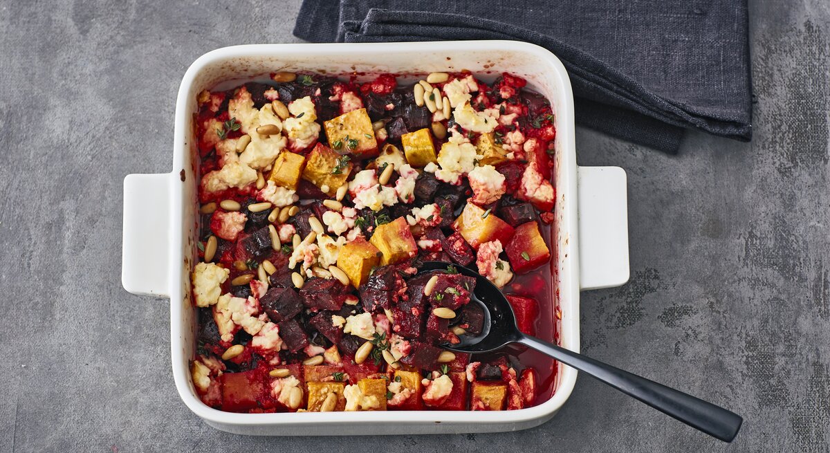 Rote-Bete Gratin mit Feta, Kürbis, Pinienkernen und Thymian in einer großen Auflaufform auf steinernem Untergrund. 