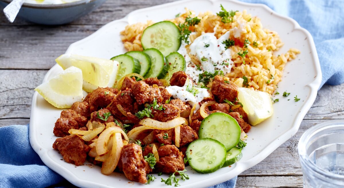Auf einem Teller ist eine Veggie-Gyros-Platte mit Gurken, Zitrone und Reis angerichtet.