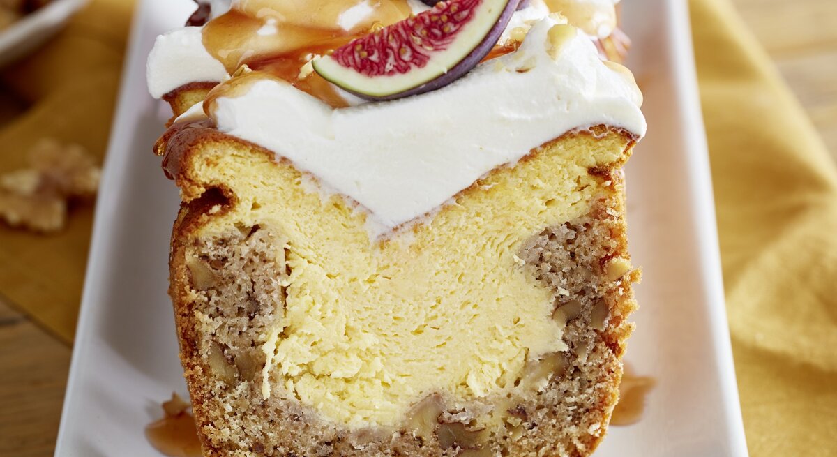Angeschnittener Feigen-Walnuss-Kuchen auf weißem Teller, im unscharfen Hintergrund Walnüsse und ein gelbes Küchentuch. 