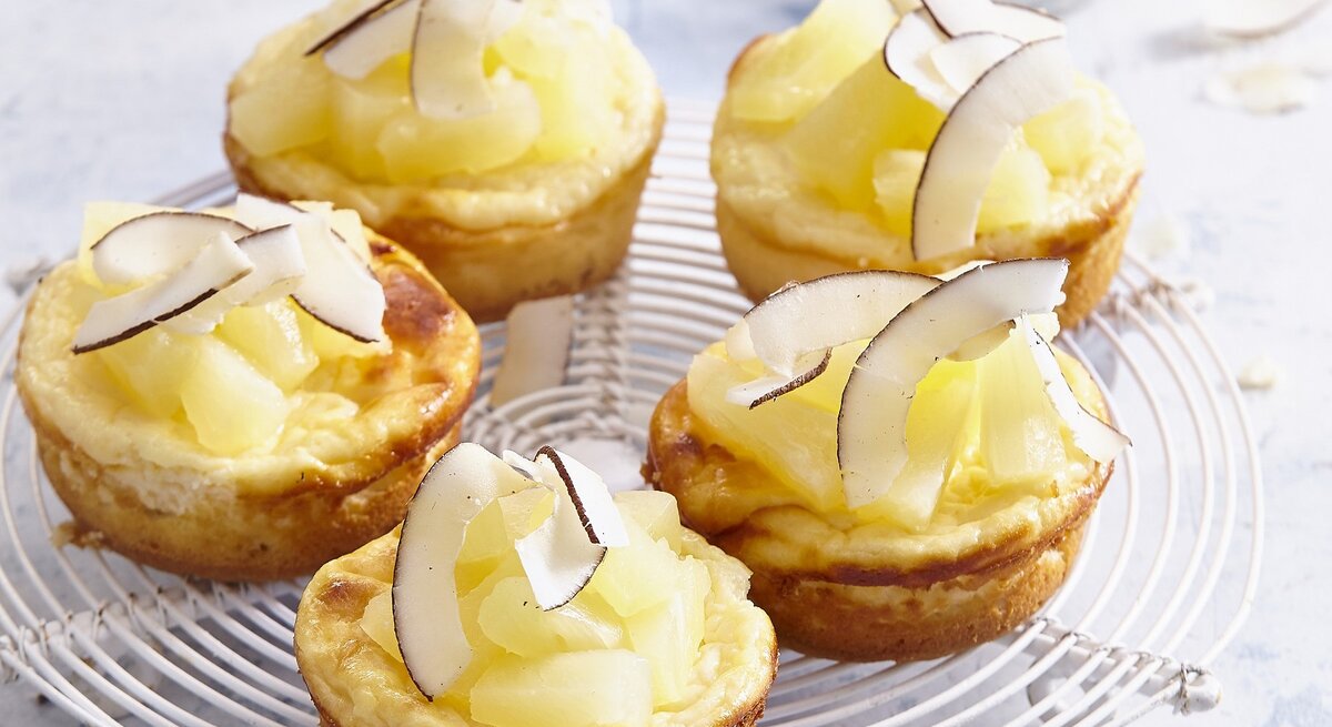 Auf einem Kuchengitter stehen mehrere Pina-Colada-Mini-Käsekuchen. Sie sind mit Kokosraspeln verfeinert. 