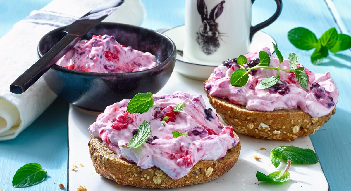 Drei Brötchen mit Beeren-Quark / Schale mit Beerenquark / Messer / Teetasse / Nahaufnahme