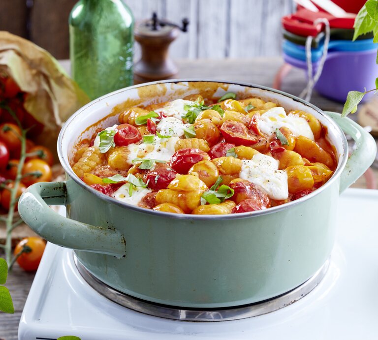 Eintopf aus Gnocchi mit Burrata und gebackenen Tomaten, bestreut mit frischem Basilikum und serviert in einem großen, hellen Kochtopf auf einem Campingtisch.   | © EAT CLUB / Isabell Triemer