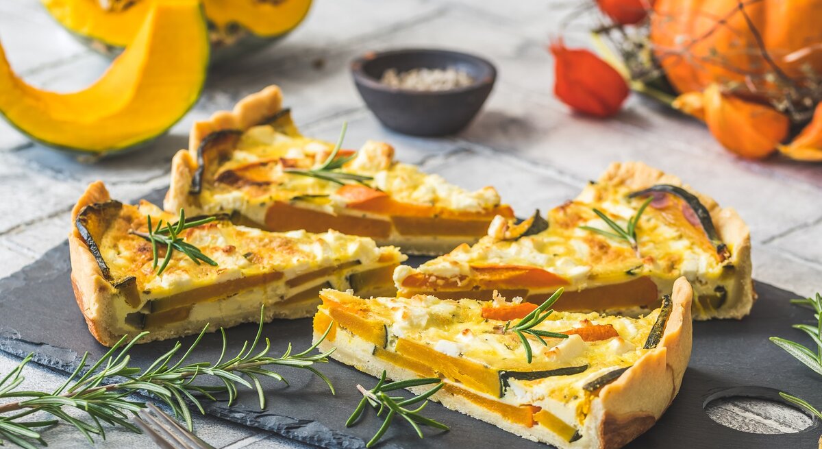 Vier Stücke Kürbis-Feta-Quiche auf einer schwarzen Schieferplatte.