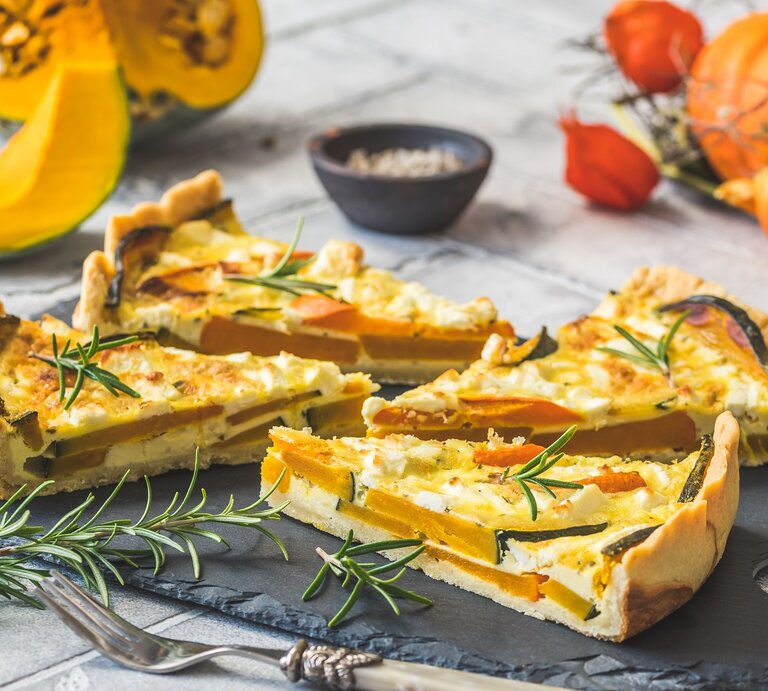 Vier Stücke Kürbis-Feta-Quiche auf einer schwarzen Schieferplatte. | © AdobeStock/Daniela Baumann