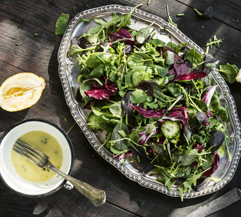 Silberne Platte mit Salat auf hölzernem Untergrund. Daneben einige ausgepresste Zitronen und eine Schale mit Buttermilch-Zitronen-Dressing.  | © Getty Images/Westend61