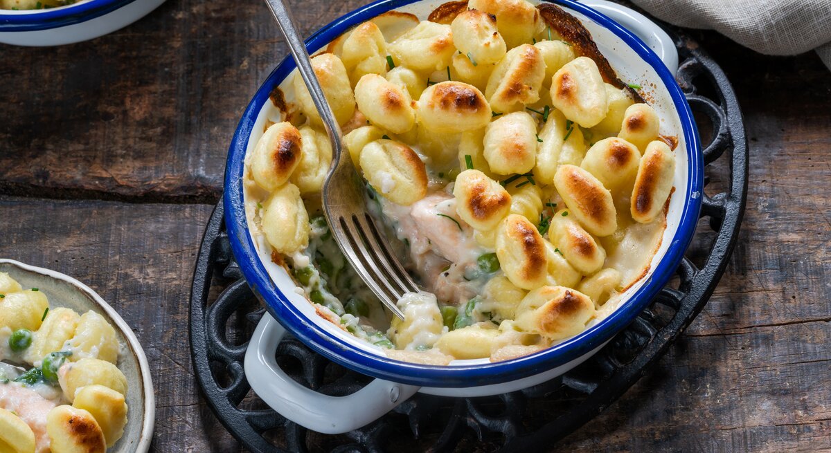 Eine blaue Form mit Gnocchi-Lachsauflauf mit Erbsen auf einem braunen Tisch.