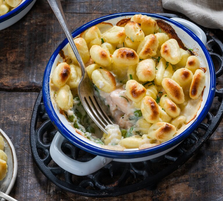 Eine blaue Form mit Gnocchi-Lachsauflauf mit Erbsen auf einem braunen Tisch. | © Adobe Stock/ beataaldridge