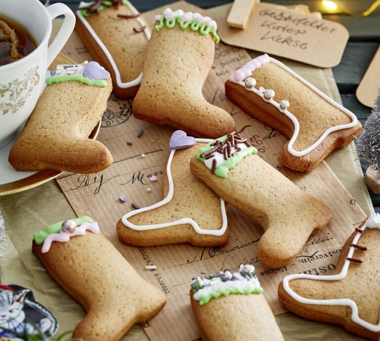 Auf einem Weihnachtstisch liegen meherer Gestiefelter-Kater-Kekse. Sie sind mit buntem Zuckerguss dekoriert. | © EAT CLUB / Isabell Triemer