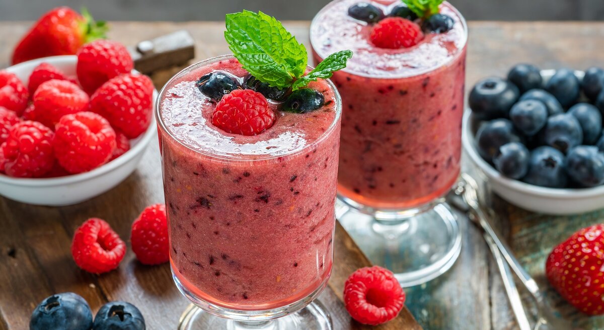 Zwei Gläser mit Beeren-Matcha-Smoothie auf einem Holztisch.
