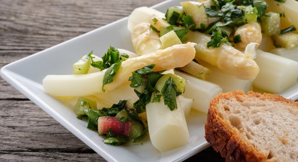 Ein weißer rechteckiger Teller mit dem Spargelsalat auf einem dunklen Holztisch.