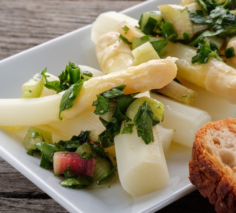 Ein weißer rechteckiger Teller mit dem Spargelsalat auf einem dunklen Holztisch. | © shutterstock/ Bernd Schmidt