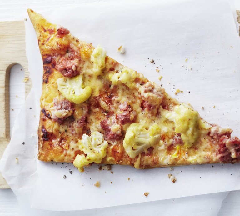 Auf einem Schneidebrett liegt ein Stück Pizza auf norddeutsche Art mit Blumenkohl und Mettwurst. Sie ist frisch gebacken, goldbraun und direkt von oben fotografiert.  | © StockFood / Gräfe & Unzer Verlag / Suedfels, Thorsten