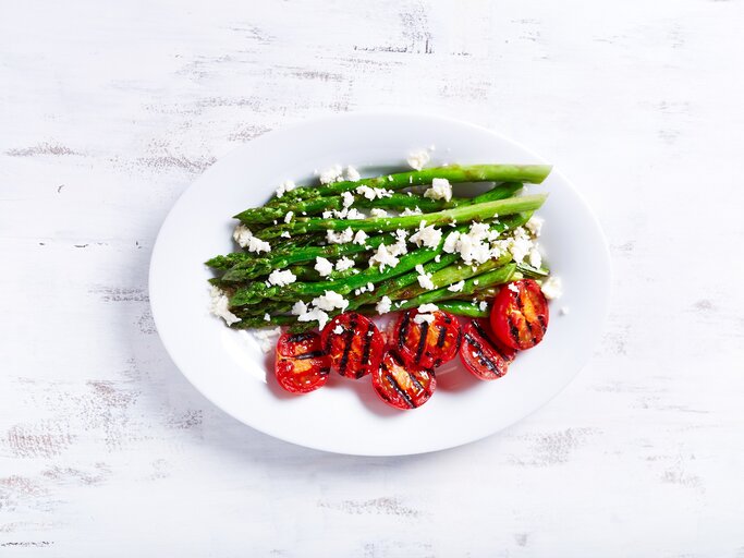 Ein Teller gegrillter Spargel mit Zitrone und Feta sowie gegrillten Tomaten in der Draufsicht. | © Adobe Stock/ B.G. Photography