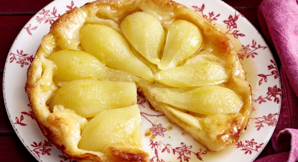Auf einem Teller liegt eine Birnen-Tarte-Tatin. Sie ist goldbraun gebacken und mit saftigen Birnen belegt.