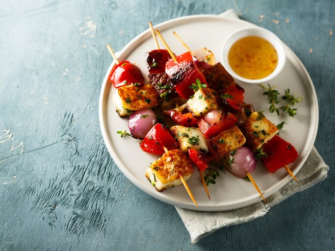 4 Tofu-Grillspieße mit Gemüse auf einem Teller, auf dem auch eine Schale mit Dip steht.  | © Adobe Stock/ marysckin