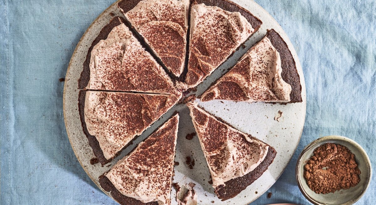 Auf einem Teller liegt ein Keto-Schokoladenkuchen. Er ist mit Kakaopulver bestreut.