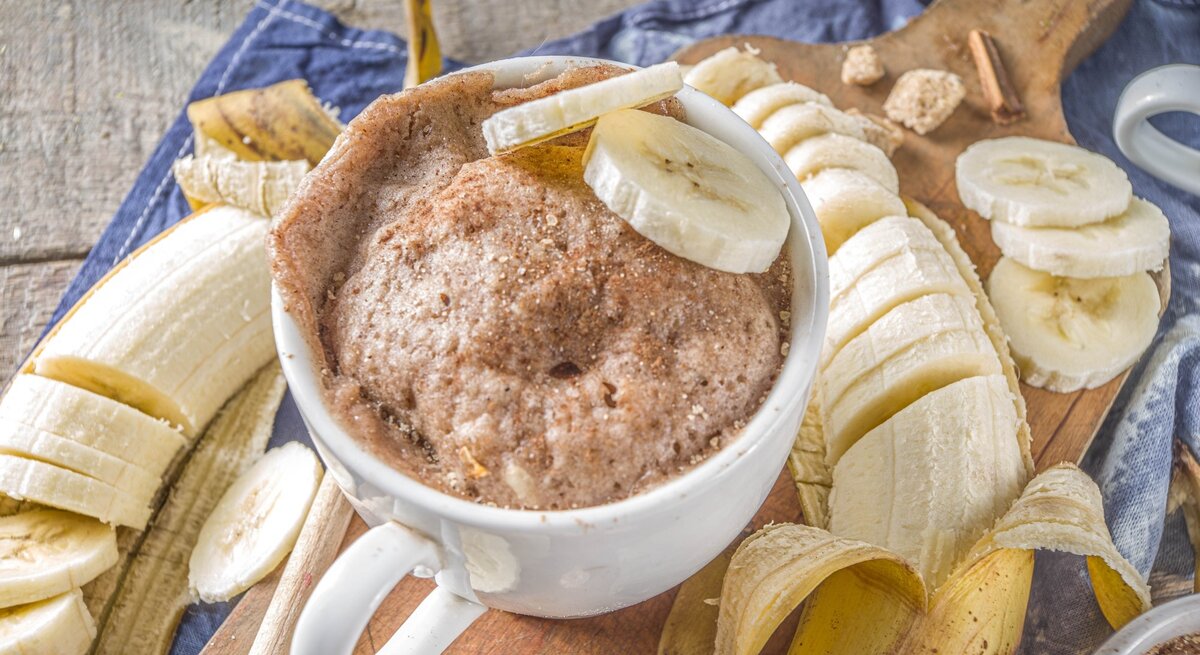 In einer Tasse ist ein Bananen-Tassenkuchen gebacken. Oben drauf liegen zwei Scheiben Bananen. Er ist mit Zimt bestreut.