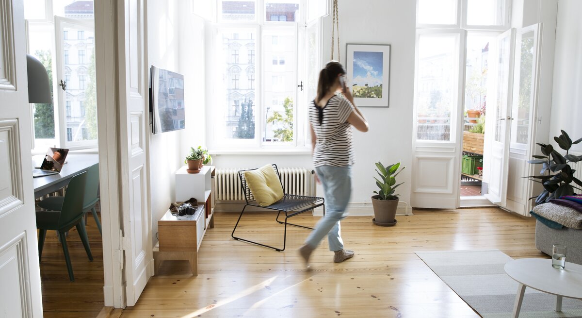 Frau läuft mit Telefon am Ohr in der Wohnung umher.