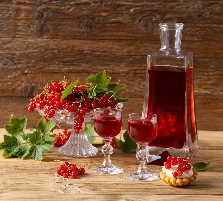 Eine Glasflasche mit Johannisbeerlikör mit Wodka auf einem Holztisch. | © AdobeStock/gkrphoto