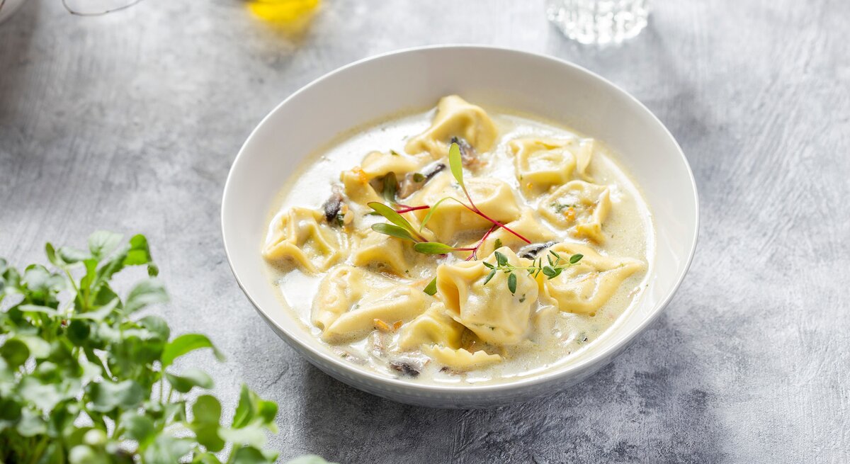 Eine weiße Schale mit der Suppe auf grauem Untergrund. Alles von schräg oben fotografiert.