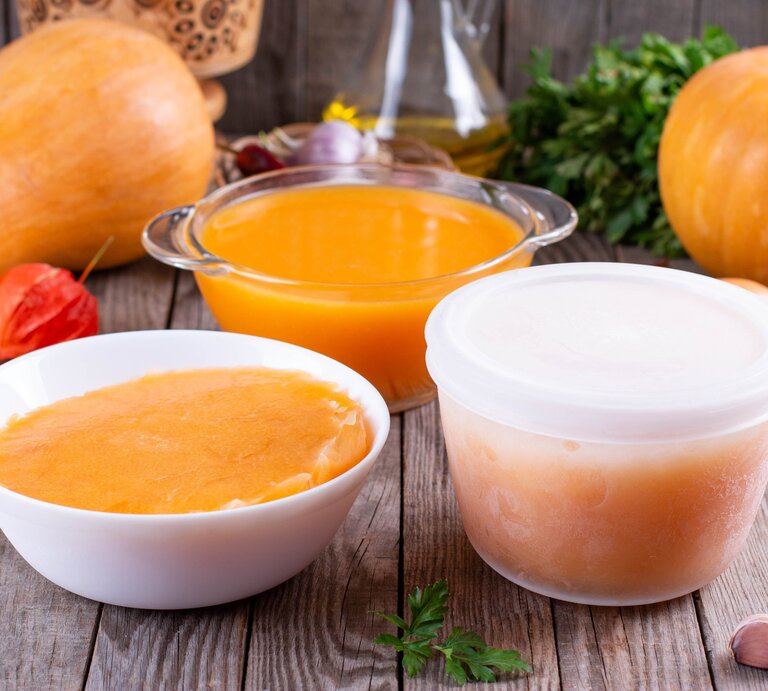 Kürbissuppe einfrieren Kürbissuppe in Gefäßen auf Holztisch. Im Hintergrund eine Karaffe mit Öl, Kürbisse und Zutaten. Frontalansicht. | © Getty Images / Qwart