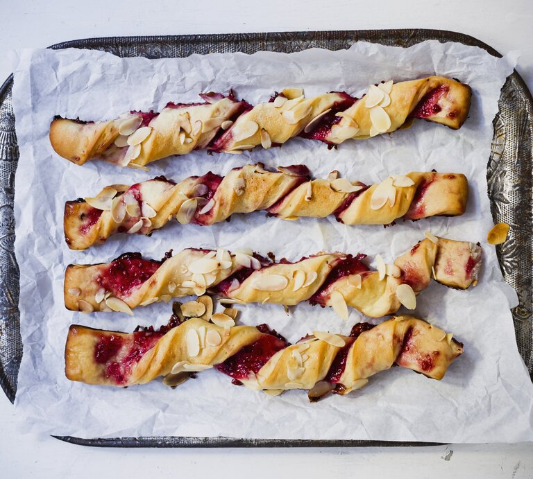 Auf einem Tablett liegen vier Rollen Blätterteigstangen mit Marmelade. Sie sind mit Mandelblättchen verziert. | © Stockfood/Sporrer/Skowronek