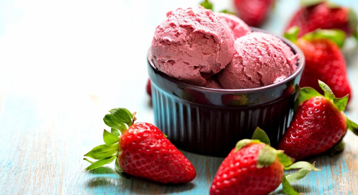 Eine Schale mit 3 Kugeln Erdbeer-Nicecream, drumherum liegen frische Erdbeeren.