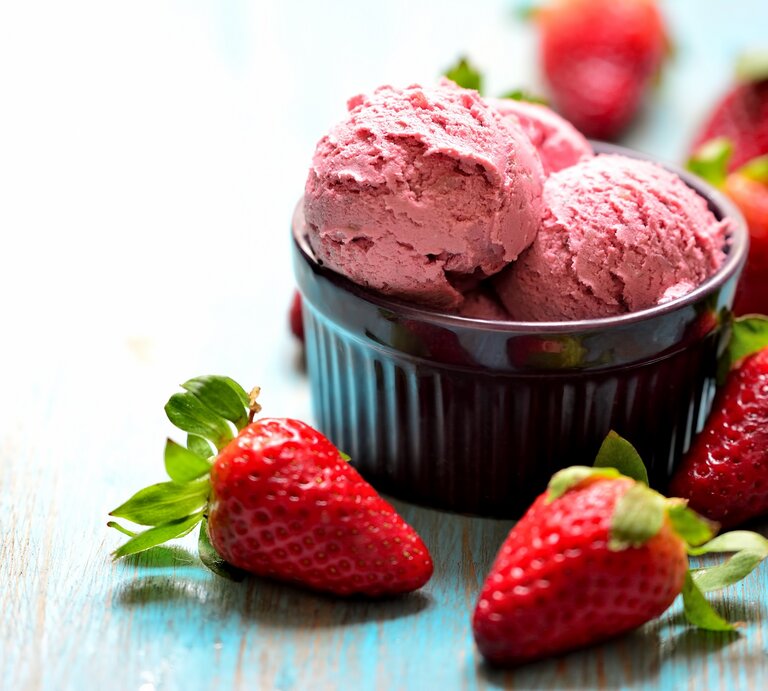 Eine Schale mit 3 Kugeln Erdbeer-Nicecream, drumherum liegen frische Erdbeeren. | © Adobe Stock/ Giovanni Cancemi