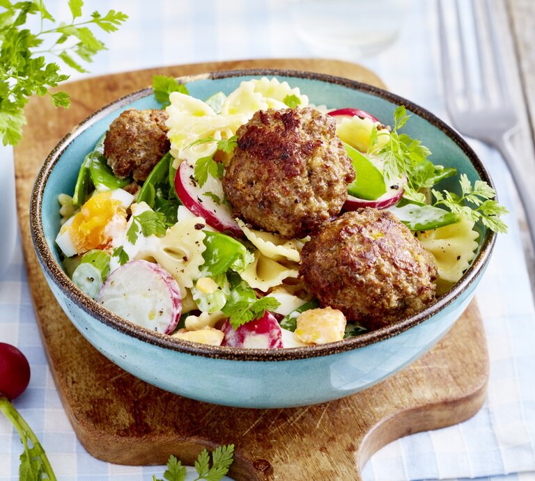 Buletten mit Nudelsalat, bestehend aus gekochten Eiern, Radieschen und Gurken, garniert mit frischem Kerbel und serviert in einer blauben Tonschale auf einem Holzbrett.  | © EAT CLUB / Isabell Triemer