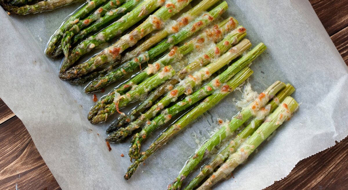 Überbackener Spargel aus dem Ofen auf einem mit Backpapier belegten Blech. Das Ganze auf einem hölzernen Untergrund.
