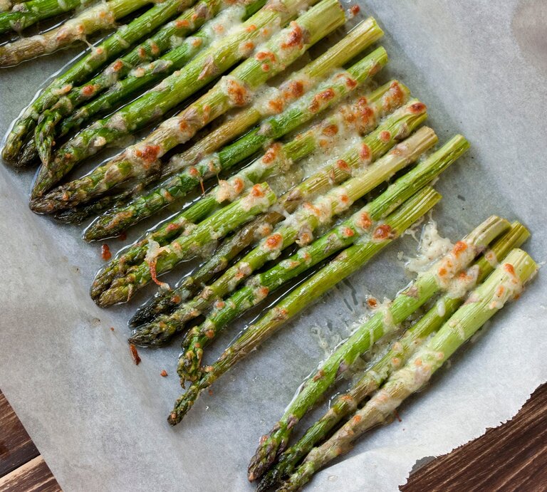 Überbackener Spargel aus dem Ofen auf einem mit Backpapier belegten Blech. Das Ganze auf einem hölzernen Untergrund. | © Shutterstock / Joanna 12