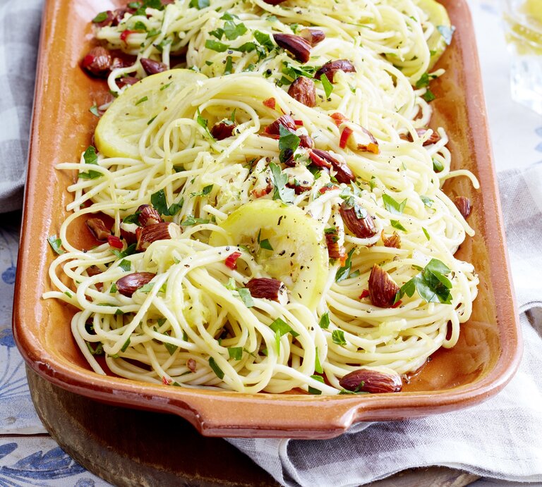 Zitronen-Mandel-Spaghetti, bestreut mit Chili und frischem Pfeffer sowie gehackter Petersilie, in einer Tonform auf gedecktem Tisch mit Tischdecke serviert.  | © EAT CLUB / Isabell Triemer