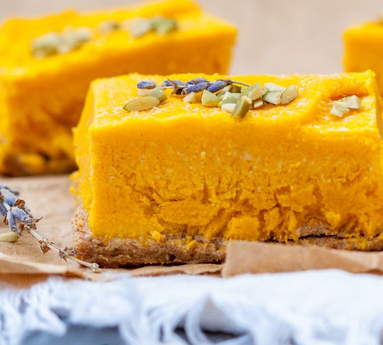 Drei Stücke von dem Kokos-Kürbis-Cheesecake auf Backpapier und einem grauen Tisch. Sehr nah von der Seite fotografiert. | © Shutterstock/ Nina Firsova 