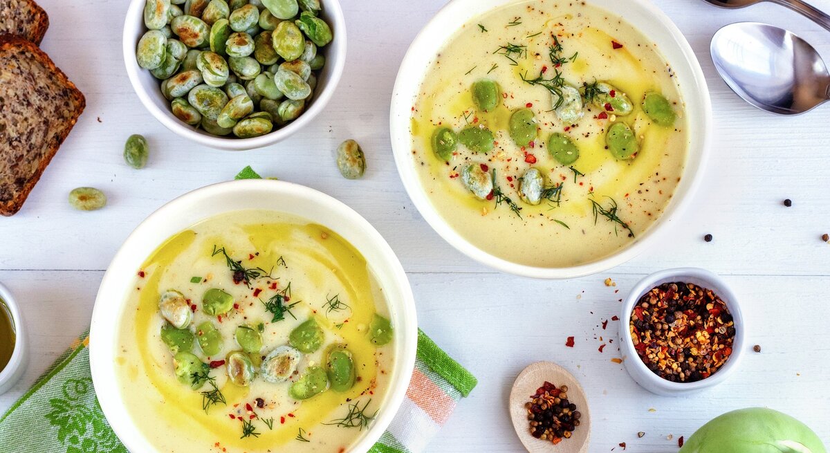 Zwei Suppenteller auf einem weißen Tisch mit Bohnen, Brot, Chilipulver und Kohlrabi.