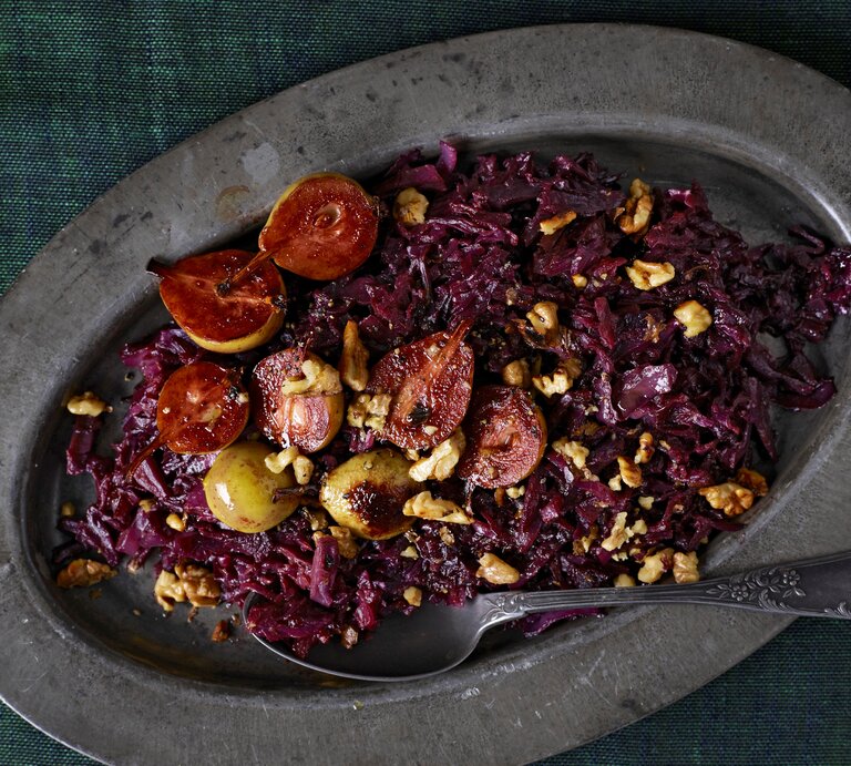 Eine ovale Platte auf der das geschmorte Rotkohl mit Birnen mit Walnüssen garniert und einem Löffel serviert wird, vor einem dunkelgrünen Hintergrund, von oben.  | © Stockfood/ Candis Magazine/ Benson, Terry