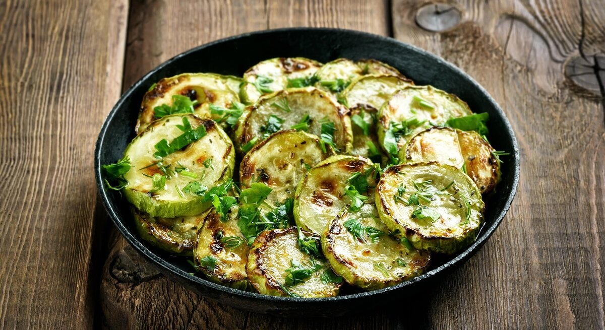 Draufsicht: Eine Pfanne frittierte Kräuter-Zucchini auf einem Untergrund aus Holz.