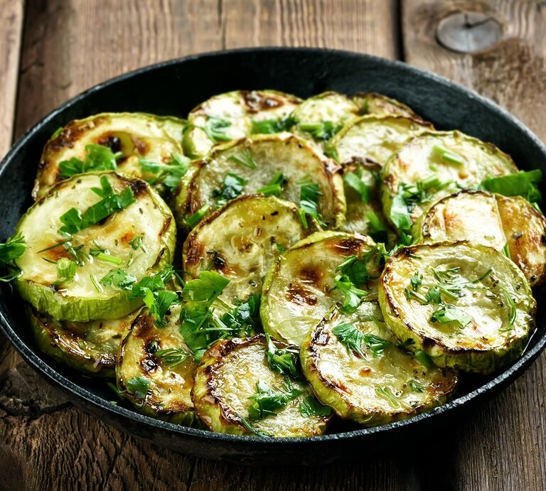 Draufsicht: Eine Pfanne frittierte Kräuter-Zucchini auf einem Untergrund aus Holz. | © Shutterstock / Tatiana Volgutova