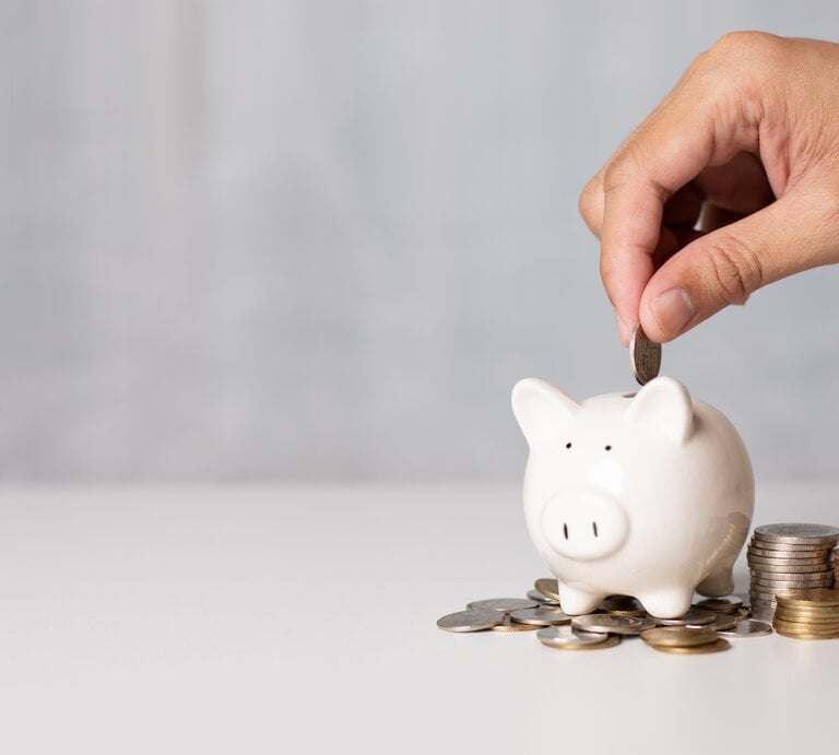 Eine Person wirft eine Münze in ein Sparschwein. | © shutterstock/Natthapol Siridech