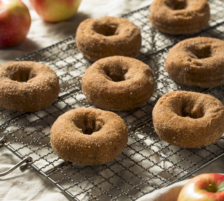Apfelwein Donuts mit Zimt auf einem Gitter neben frischen Äpfeln auf einer hellen Tischdecke.  | © Getty Images / bhofack2