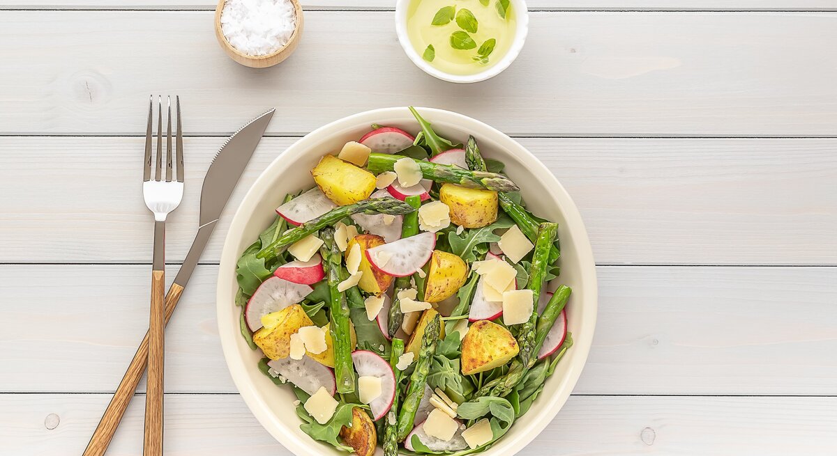 Eine Schale gegrillter Spargel-Kartoffel-Salat mit Radieschen und Rucola, daneben Besteck und eine schale Salz und Dip. Draufsicht.