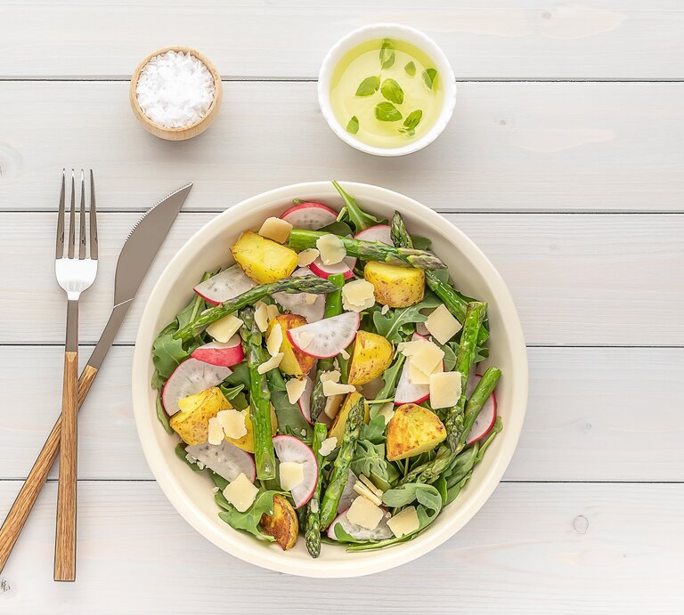 Eine Schale gegrillter Spargel-Kartoffel-Salat mit Radieschen und Rucola, daneben Besteck und eine schale Salz und Dip. Draufsicht. | © Adobe Stock/ Jane Vershinin