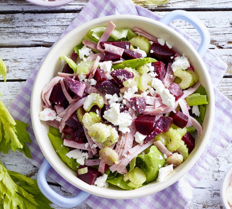 Salat mit Rote Bete und Schinken, getoppt mit frischem Feta und Sellerie, serviert in einer großen weißen Schale mit Henkeln auf einem Holztisch.  | © EAT CLUB / Isabell Triemer